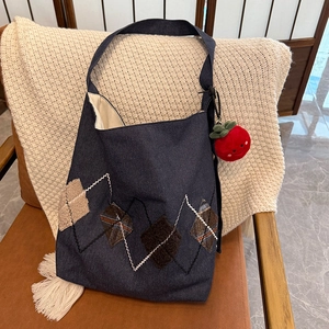 Detail of dark blue denim hobo bag with plaid patchwork and red plush smiley charm