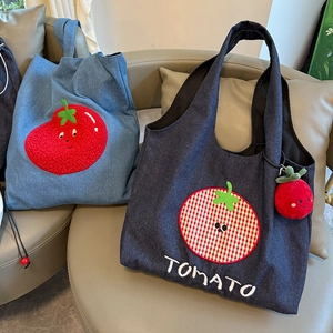 Detail of denim tote bags with tomato embroidery and cute plush keychain accessory