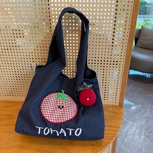 Close-up of dark denim tote bag featuring tomato embroidery and plush charm on wood table