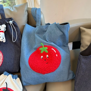 Detail of denim tote bag with cute red tomato patch on a soft gray leather sofa