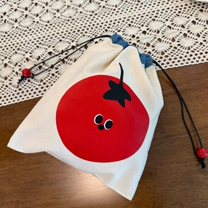 Detail of canvas drawstring bag featuring a red tomato print and blue trim detail