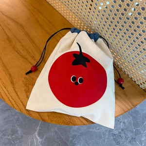 Close-up of drawstring canvas bag with red tomato embroidery on a wooden table