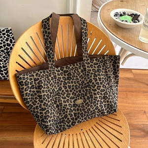 Detail of leopard print canvas tote bag featuring handmade metal logo and sturdy straps