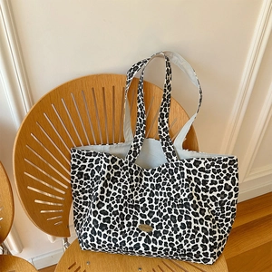 Leopard print canvas tote bag with gold metal logo tag on a modern wooden chair