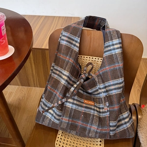 Macro detail of plaid wool blend tote bag with brown leather tag on a wooden chair