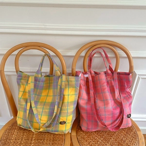 Detail of plaid canvas tote bag with check pattern on a woven chair with soft lighting