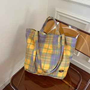 Detail of yellow and purple checkered canvas tote with dual handles and brand leather patch