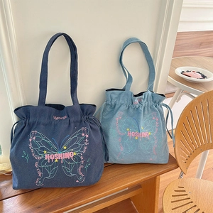 Detail of denim tote bag showing butterfly embroidery and drawstring closure texture