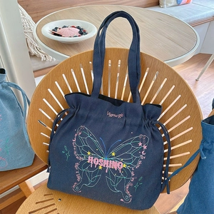 Detail of blue denim tote bag with butterfly embroidery and drawstring side design