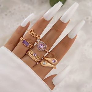 Close-up of five-piece gold ring set with purple gemstones and Love lettering on hand