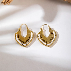 Detailed shot of golden bohemian shield earrings with white woven rope trim and metal texture