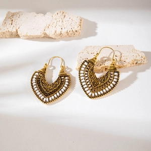 Detail of bohemian gold hollow earrings with white beads on a natural stone base