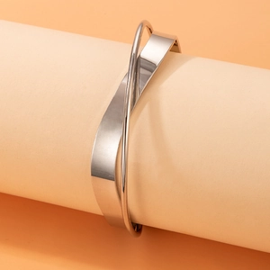 Close-up of silver criss-cross bangle featuring a wide flat band and a thin round wire
