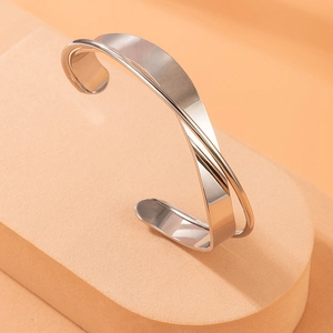Minimalist silver crossover cuff bracelet with polished geometric lines on orange display