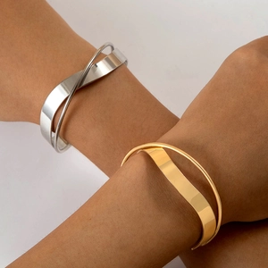 Close-up of minimalist crossover cuff bracelets in polished gold and silver finishes
