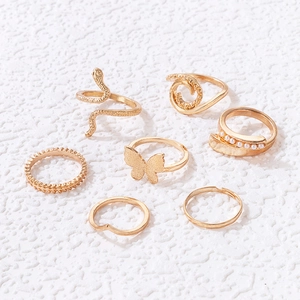 Set de 7 bagues dorées comprenant un serpent, un papillon et des perles sur fond blanc