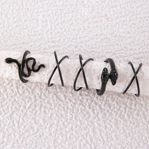 Set of five black punk snake rings and X-shaped geometric bands on a textured stand