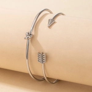Détails des bracelets argentés avec nœud et flèche sur un support beige minimaliste