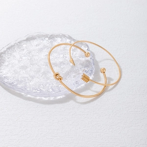 Détail de bracelets ouverts dorés avec nœud et flèche sur une surface en verre texturé