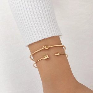 Ensemble de deux bracelets dorés avec nœud et flèche portés au poignet d'une femme