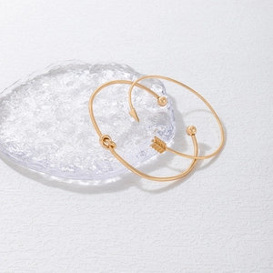 Ensemble de bracelets ouverts dorés avec nœud et flèche sur un plateau en verre chic