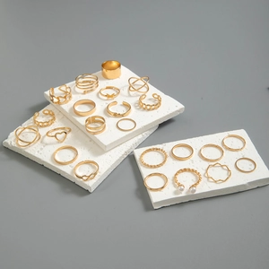 Detailed view of 20-piece gold butterfly and heart ring set on white textured stone pedestals