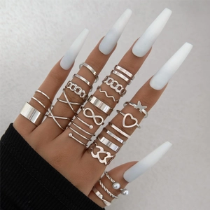 Close-up of stacked silver rings with butterfly and heart charms on a hand with white nails
