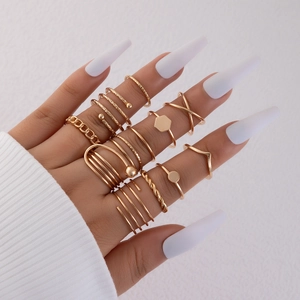 Detail of stacked gold geometric rings with chain link and cross designs on a model hand