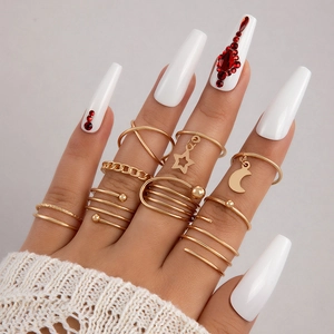 Close-up of a stacked gold ring set with star and moon charms on hand with red nails