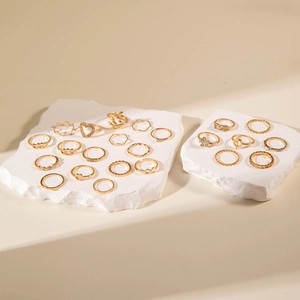 Flat lay of gold fashion ring set with heart and leaf designs on stone platform
