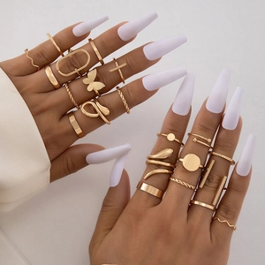 Close-up of gold butterfly and geometric knuckle ring set worn on fingers with white nails