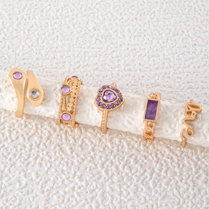 Detail of 5-piece gold-tone ring set with purple crystals on a textured display