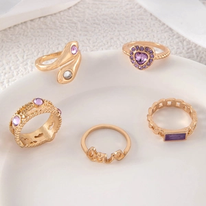 Detail shot of 5-piece gold-tone ring set featuring purple gemstones and Love lettering
