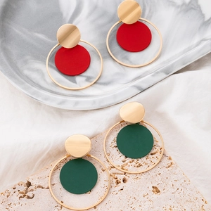 Detalle de pendientes geométricos rojos y verde oscuro en una bandeja de mármol real