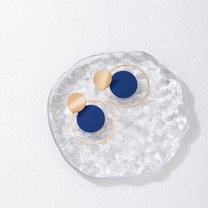 Detalle de pendientes geométricos dorados y azul marino sobre una bandeja de cristal