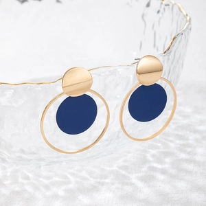 Detalle macro de pendientes geométricos con aros dorados y discos en azul marino