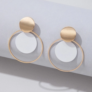 Detalle de pendientes geométricos con aro dorado y colgante circular blanco puro