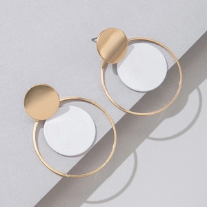 Detalle de pendientes geométricos de metal dorado y discos blancos mate de estilo moderno
