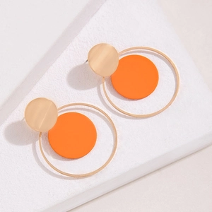 Detalle de pendientes geométricos con discos naranjas y círculos metálicos dorados en capas