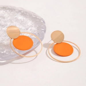Vista detallada de pendientes geométricos dorados con discos naranjas brillantes
