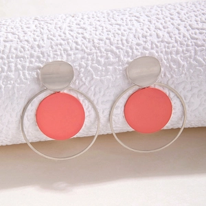 Detalle macro de pendientes de aros plateados con disco rojo coral mate geométrico