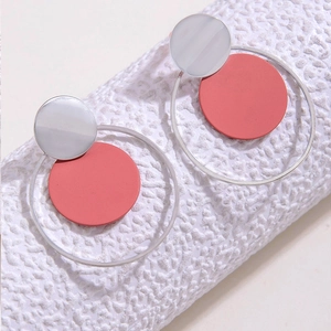 Detalle de pendientes geométricos redondos con aros plateados y disco de rojo coral