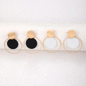 Detalle de pendientes geométricos dorados con discos negros y blancos en aros