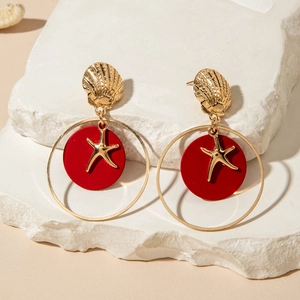 Detalle de pendientes náuticos de concha dorada con placas rojas y colgantes de estrella