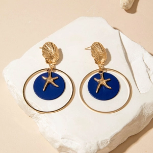 Detalle de aretes de concha dorada con dijes azul mate y acentos de estrellas de mar