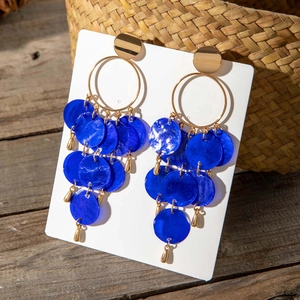 Detalle de pendientes bohemios dorados con discos de resina azul y colgantes de gota de agua