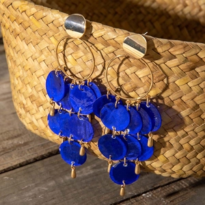 Detalle de aros bohemios dorados con lentejuelas azules colgados en una cesta tejida