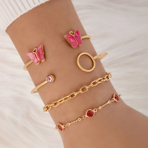 Détail d'un ensemble de 5 bracelets dorés avec papillons roses et gemmes sur le poignet