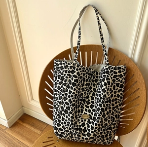 Close-up of handmade metal plaque on leopard print canvas tote bag on wooden chair