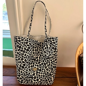 Detail of leopard print canvas tote bag with handmade metal badge on wooden surface